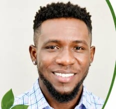 Portrait of a smiling man with dark curly hair wearing a light blue checkered shirt against a white background with green leaf accents