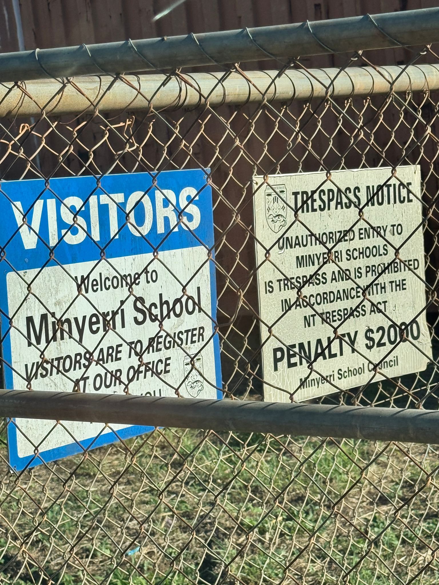 Two signs attached to a chain-link fence: a blue Visitors welcome sign for Mayvert School and a trespass notice warning of $200 penalty