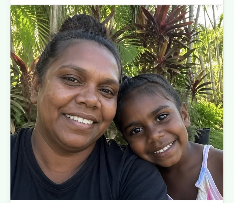 Woman and young girl smiling at the camera outdoors with tropical plants in the background