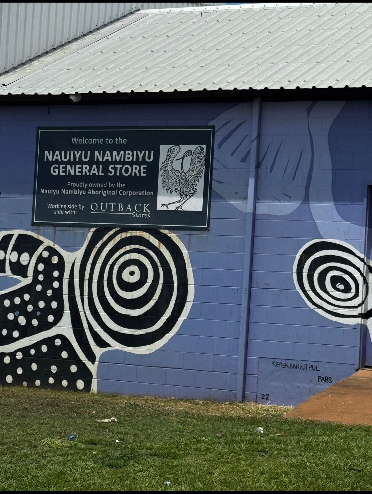 Blue building exterior with white metal roof and Aboriginal dot painting mural, Nauiyu Nambiyu General Store sign