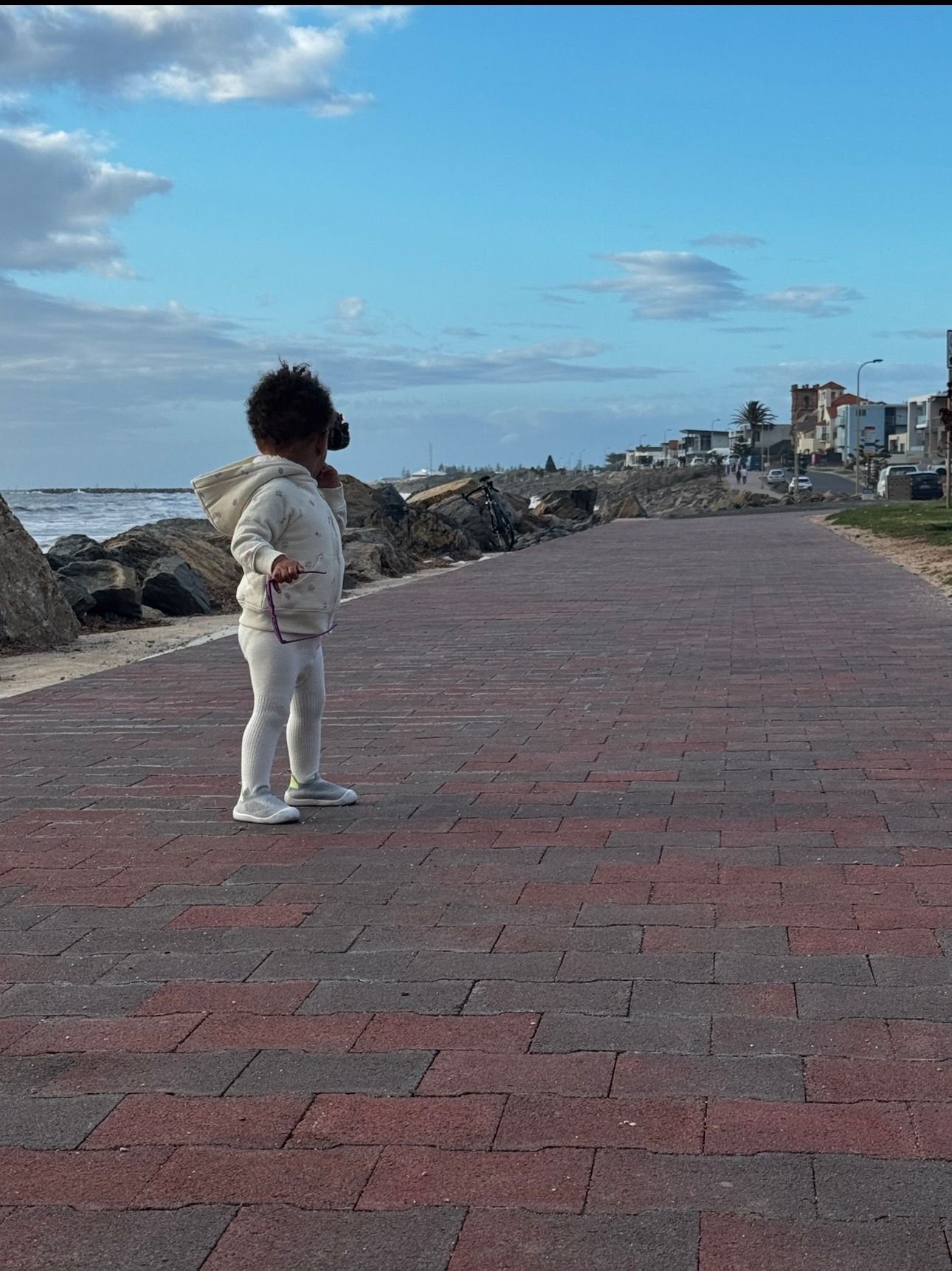 Person standing on a red brick seaside promenade looking out at the ocean and coastal town