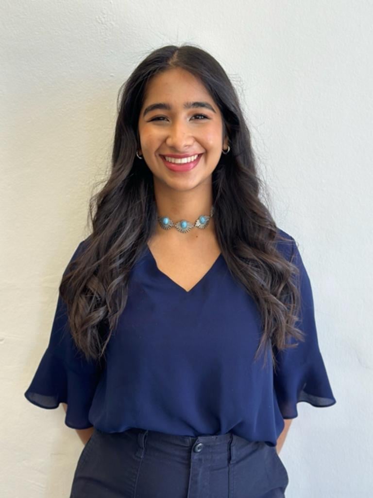 Young woman smiling at camera wearing navy blue v-neck shirt and turquoise beaded necklace