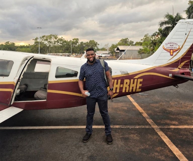 Man in dark clothing standing beside a red and white small aircraft at an airfield