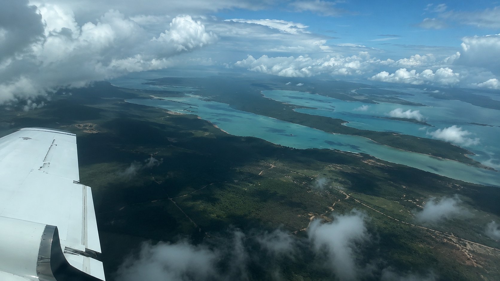 Aerial view from aircraft showing turquoise lagoon, islands, and white clouds over tropical landscape