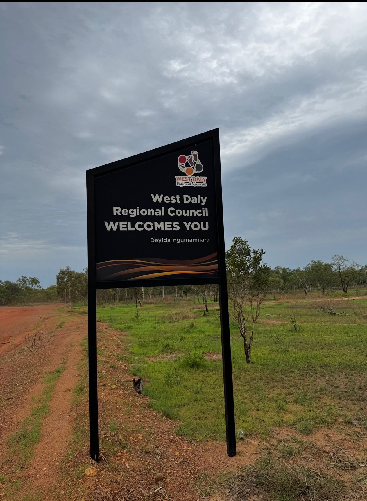 West Daly Regional Council welcome sign on a dirt road with sparse green vegetation and cloudy sky