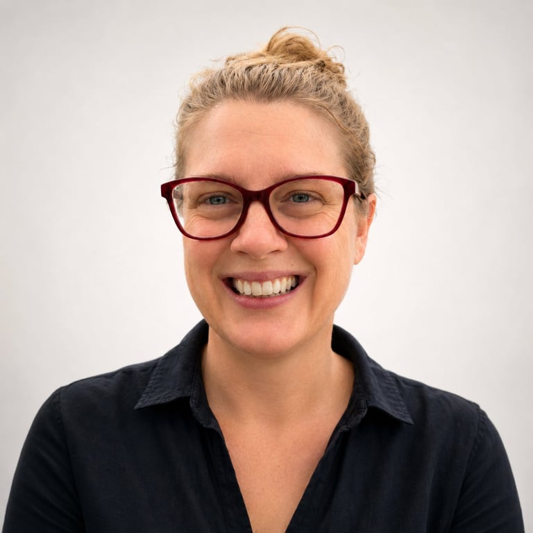 Smiling woman with blonde hair in a top bun, wearing brown glasses and a dark blue shirt against a white background